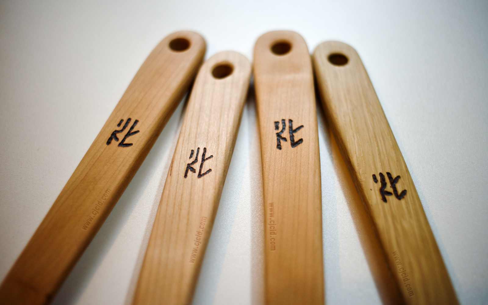 Close up on the neck’s engraved stamp of four cooking spatulæ, made from single blocks of solid Sakura or Oak woods